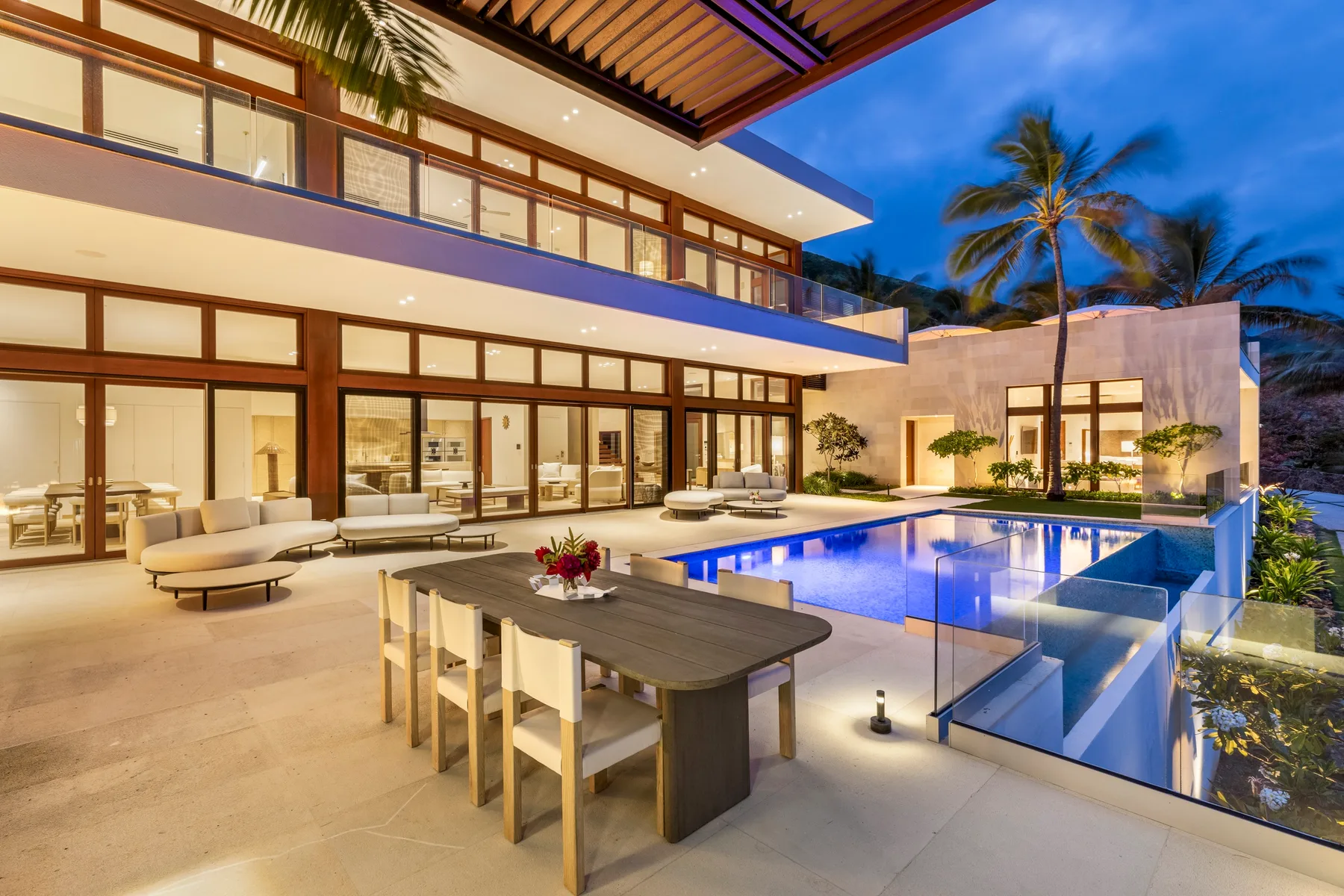 A modern house opens onto a poolside terrace with an outdoor dining table.