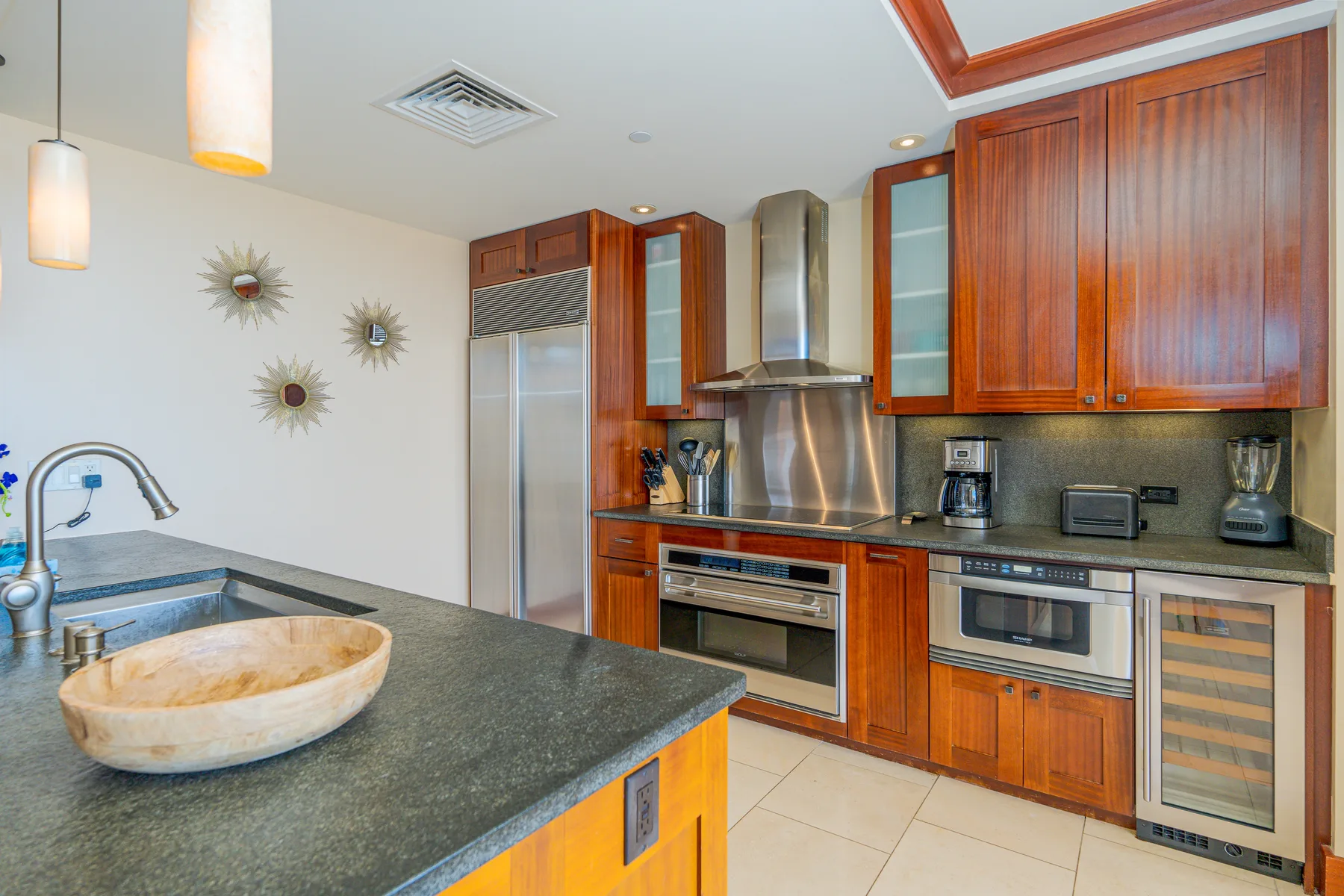A modern kitchen with wooden cabinets, stainless steel appliances, and a stone countertop.