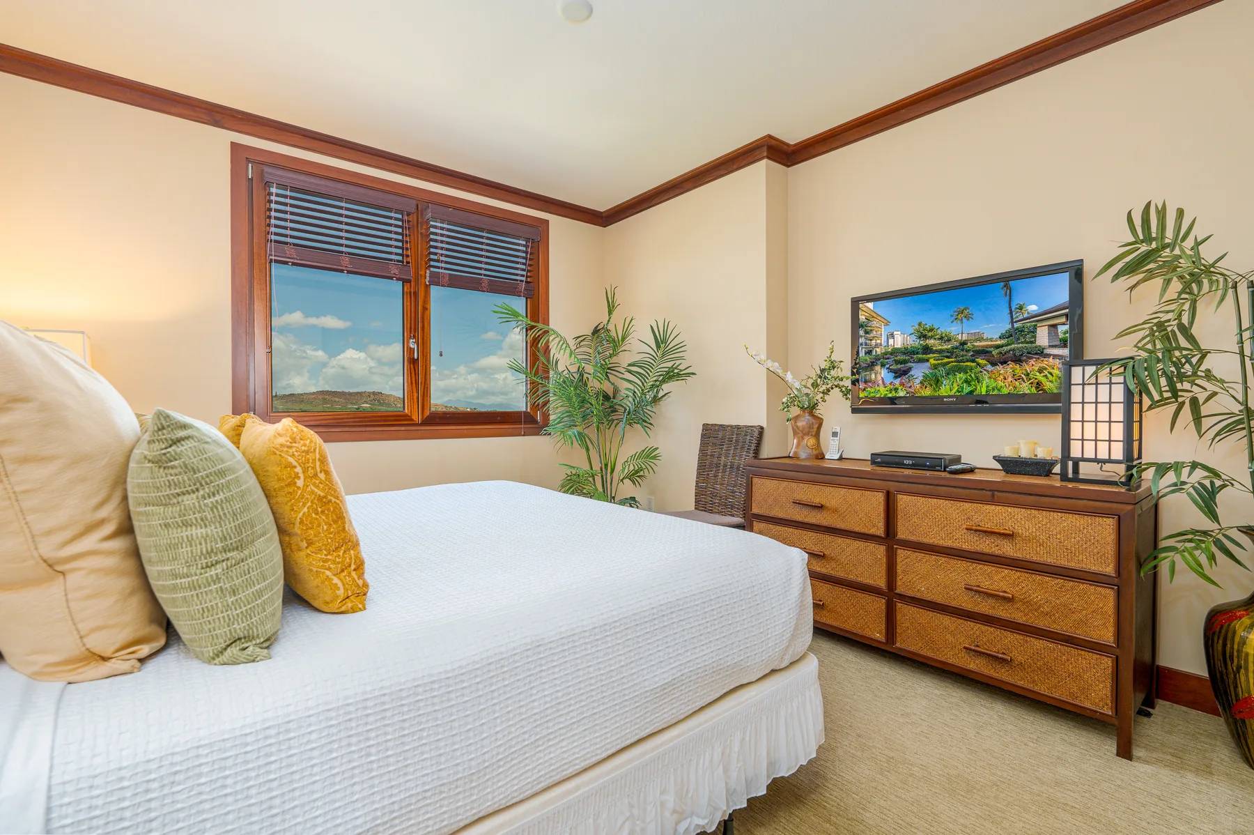 A bedroom with a bed, a wooden dresser, and plants beside the window.
