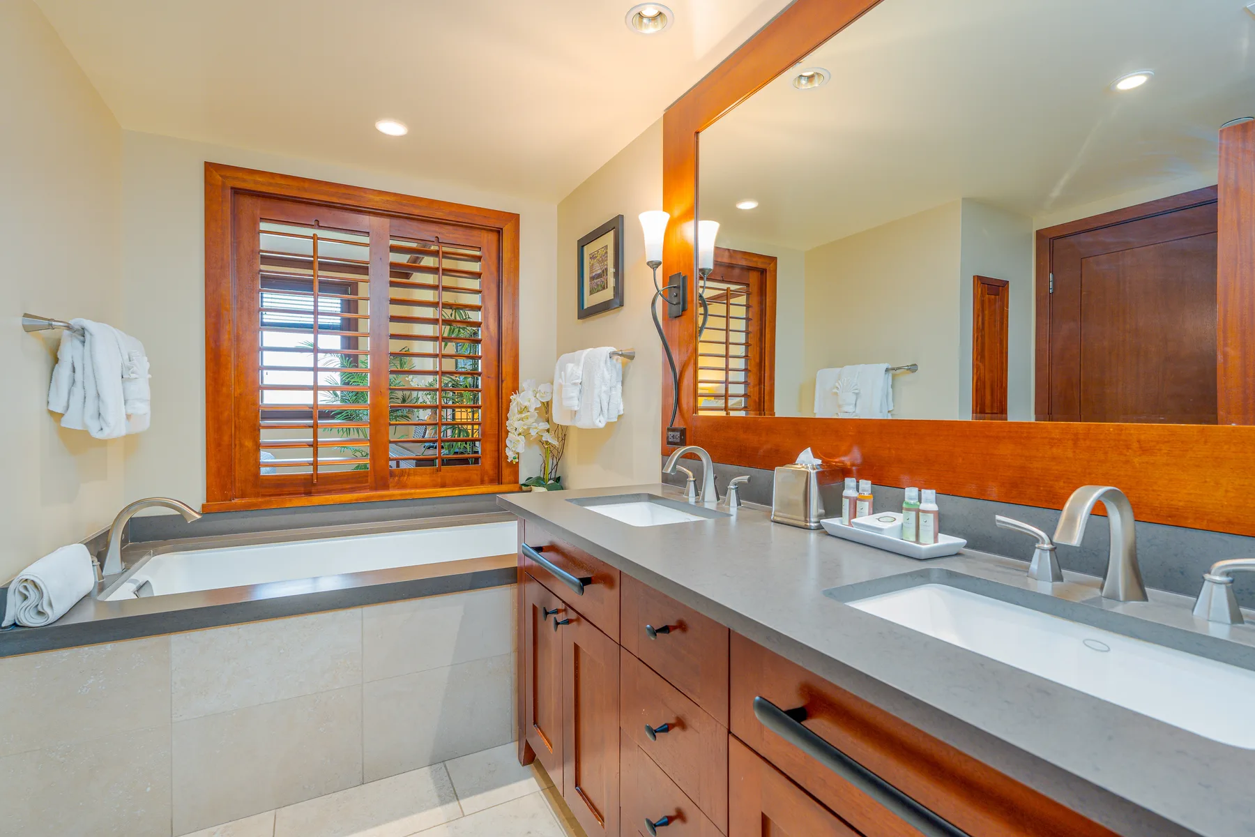 A bathroom vanity with a wide mirror and a window with wooden blinds.