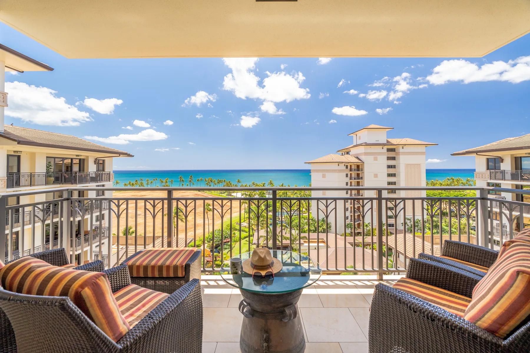 A balcony seating area overlooks nearby buildings, palm trees, and the ocean.