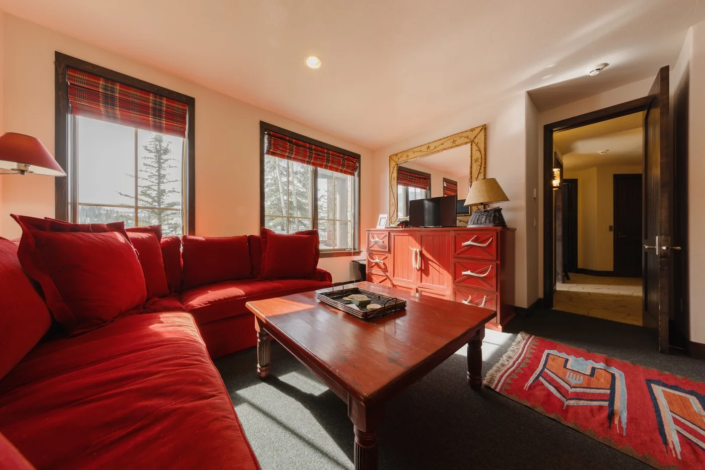 Una sala de estar con asientos rojos, una mesa de centro de madera y ventanas.