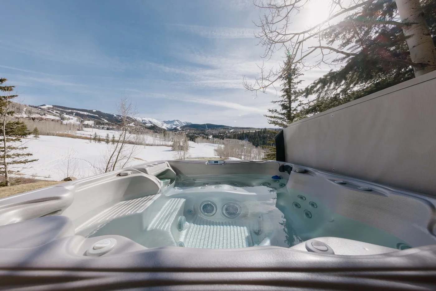 Un jacuzzi al aire libre mira hacia un paisaje nevado y montañas lejanas.