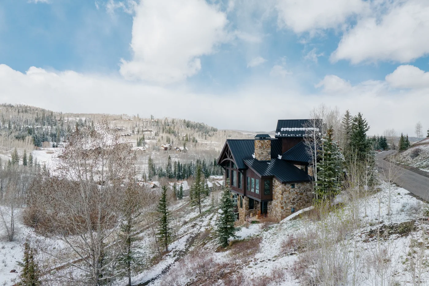 Una casa de montaña se encuentra entre árboles nevados bajo un cielo parcialmente nublado.