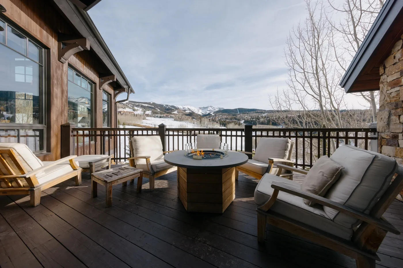 Una terraza de madera con asientos y una mesa redonda da a un paisaje nevado.