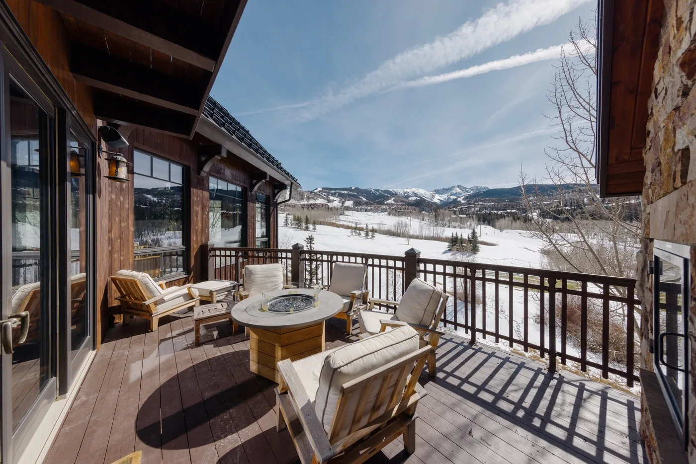 Una terraza de madera con asientos al aire libre da a un paisaje montañoso nevado.