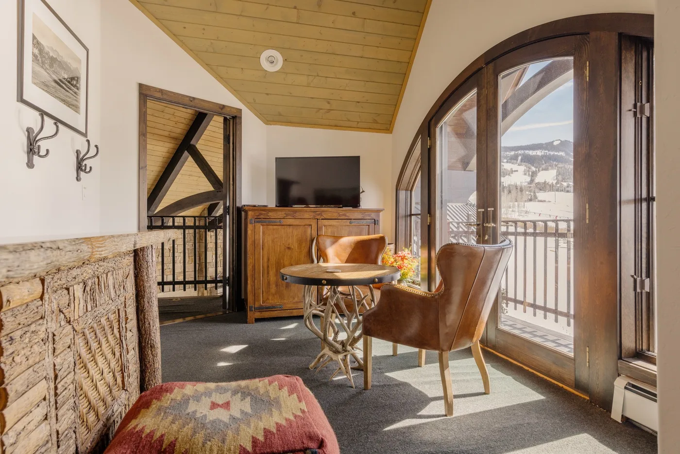 Una zona de estar con televisor y sillón junto a puertas arqueadas de vidrio.