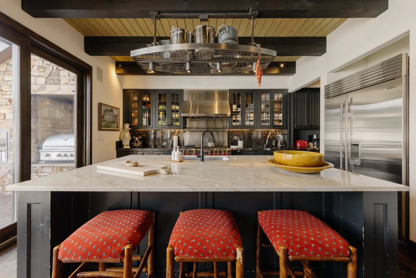 Una cocina amplia tiene una isla central con asientos tapizados en rojo.