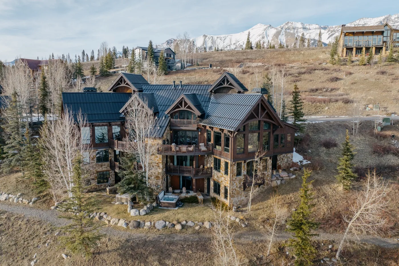 Un gran edificio de estilo albergue está rodeado de árboles, con montañas nevadas al fondo.