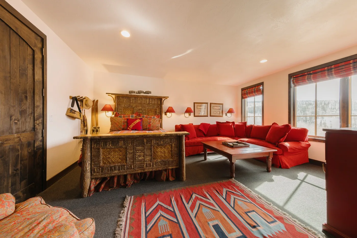 Una sala de estar con asientos rojos, una mesa de centro de madera y una alfombra estampada.