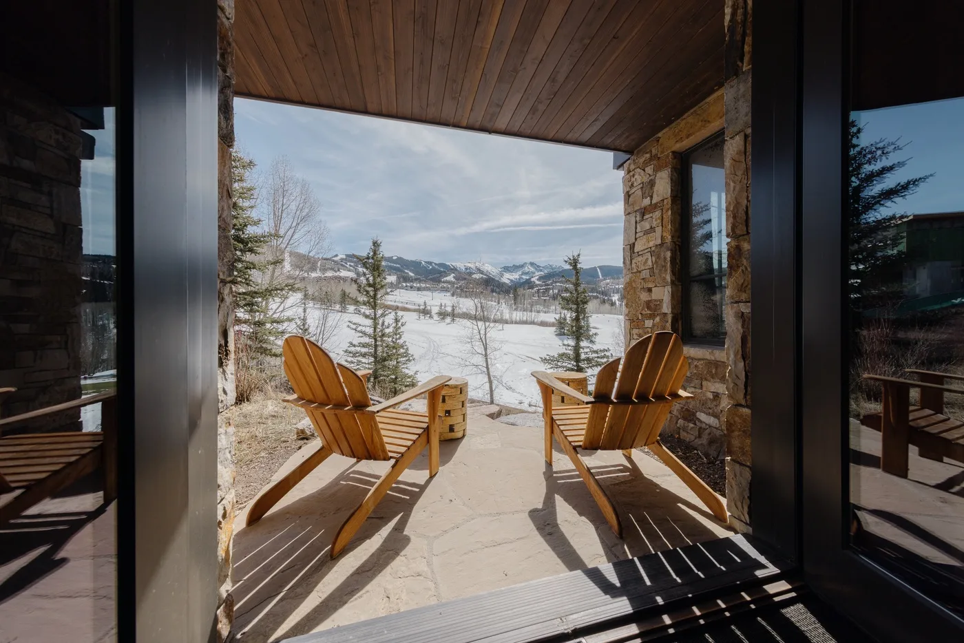 Un patio cubierto con asientos de madera da a un paisaje nevado de montaña.