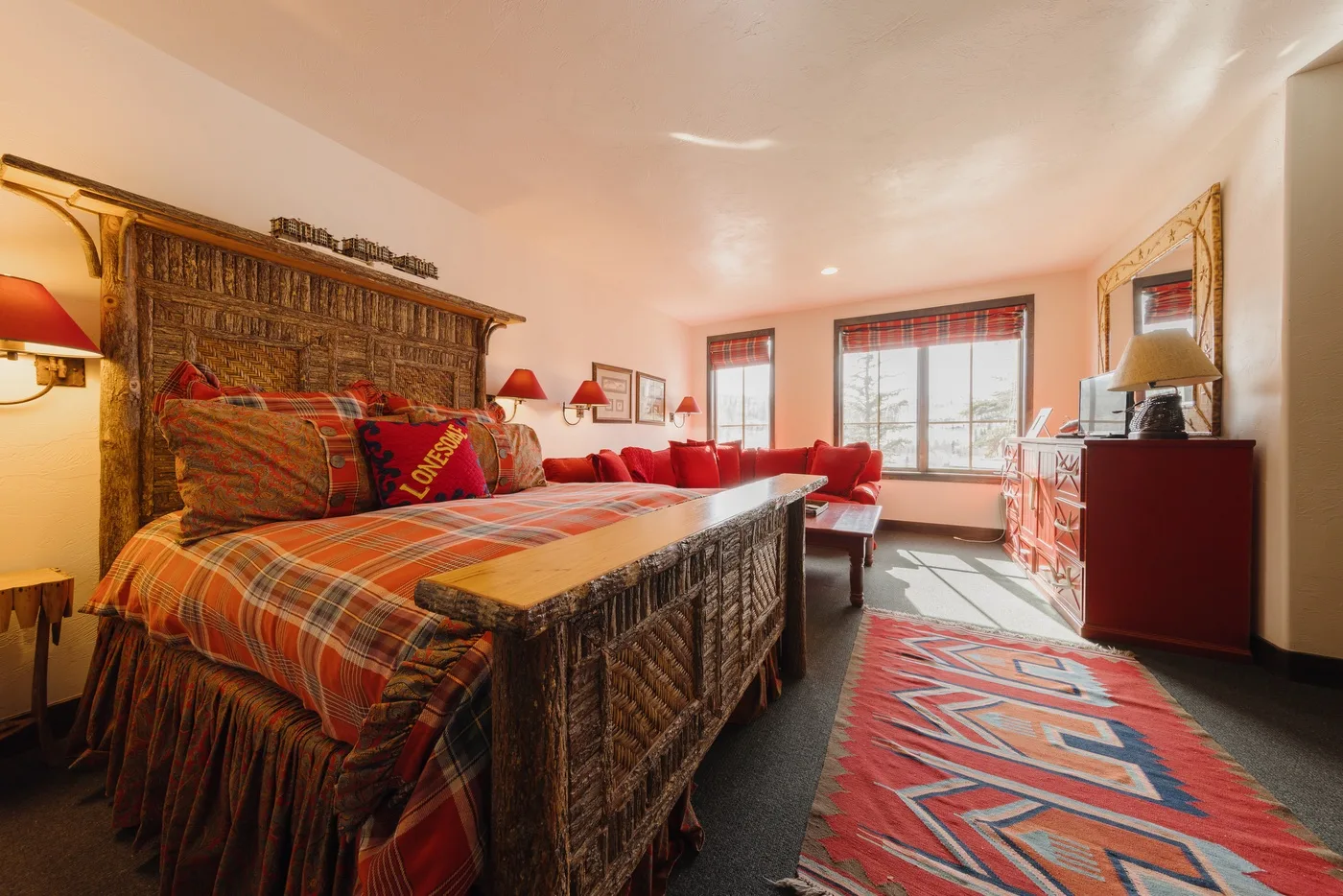 Un dormitorio cálidamente decorado, con una colcha a cuadros, asientos rojos y grandes ventanas.