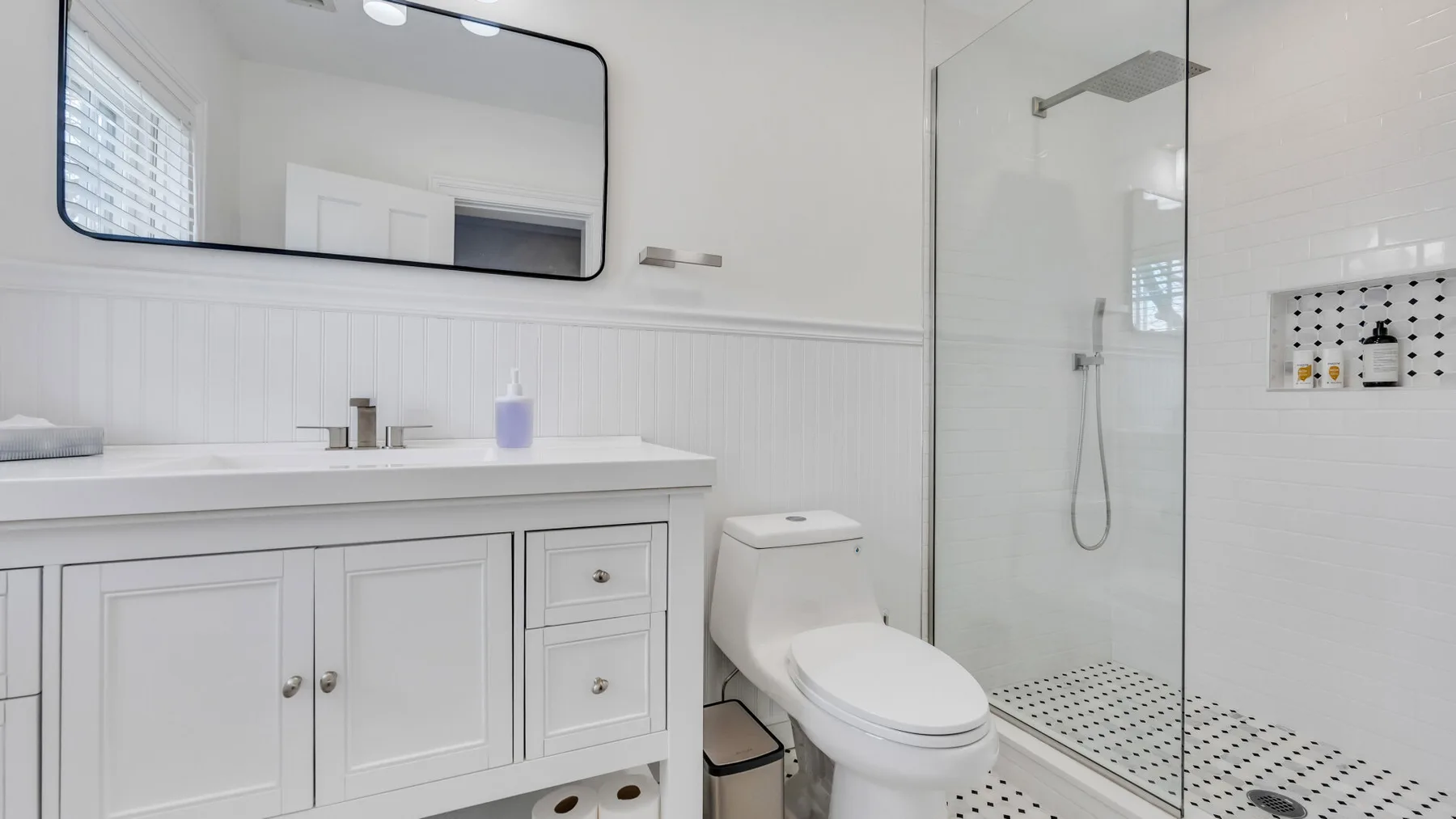 A bright bathroom with a long vanity, toilet, and glass shower.