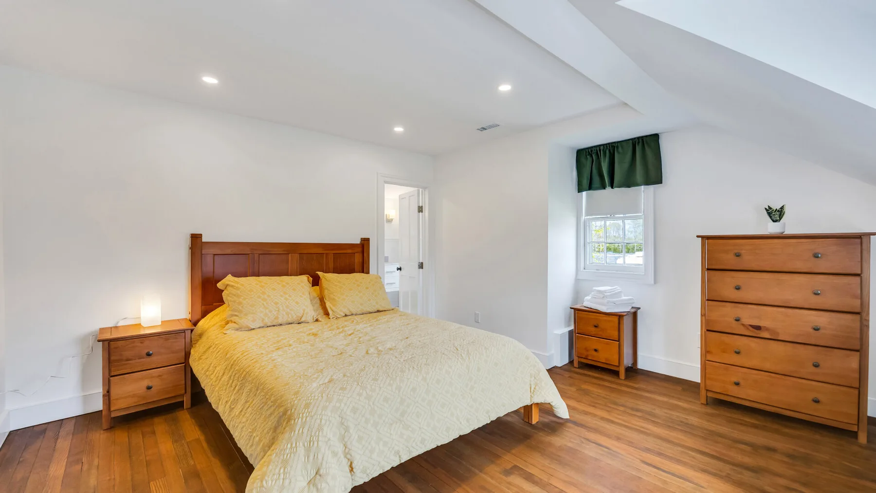 A bedroom with a bed, wooden dressers, and a window.