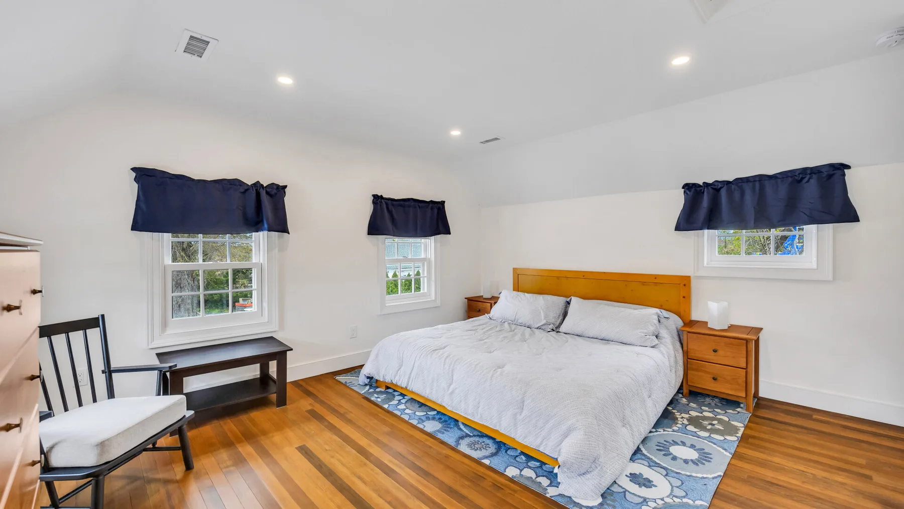 A bedroom with a bed, dark curtains, and wooden flooring.
