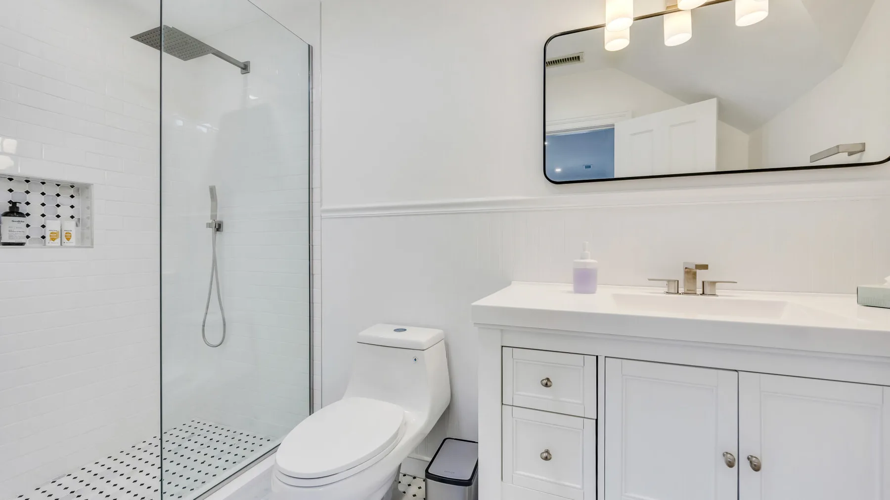 A bright bathroom with a glass shower, toilet, and white vanity.