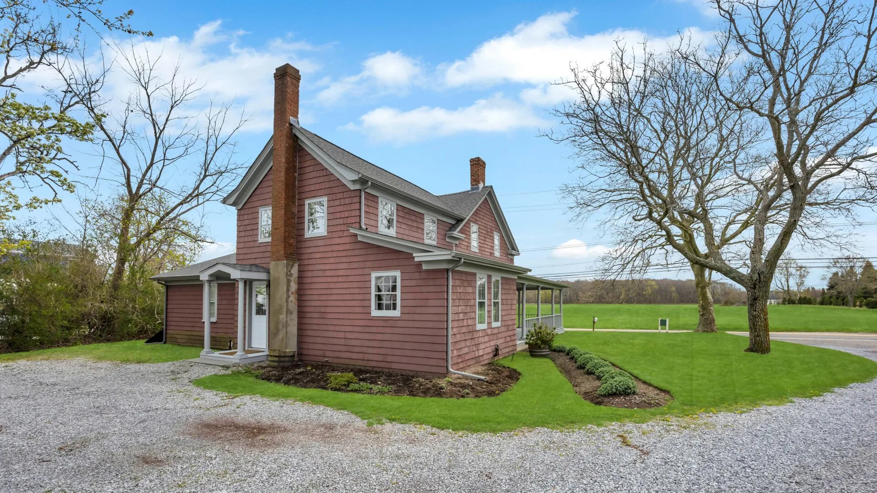 A red two-story house stands beside a gravel drive and open lawn.
