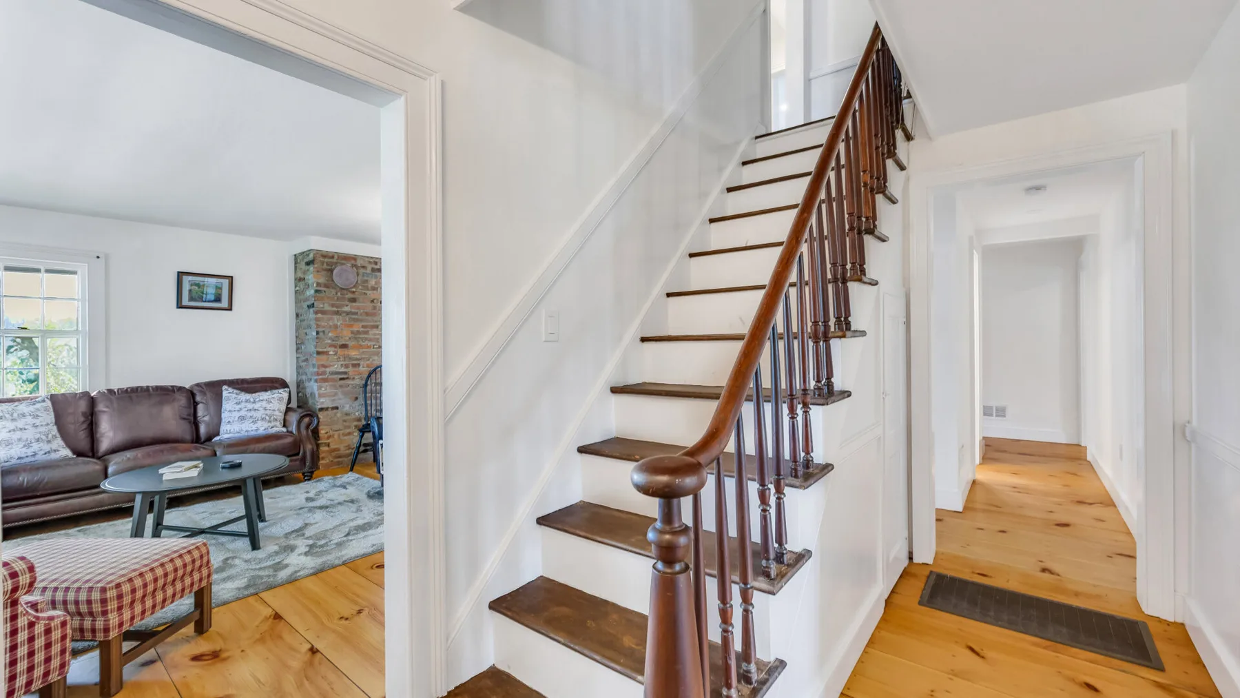 A bright interior hallway with a wooden staircase and an adjoining living room.