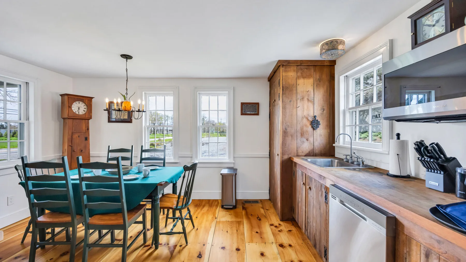 A bright dining area beside a kitchen, with a wooden table and large windows.