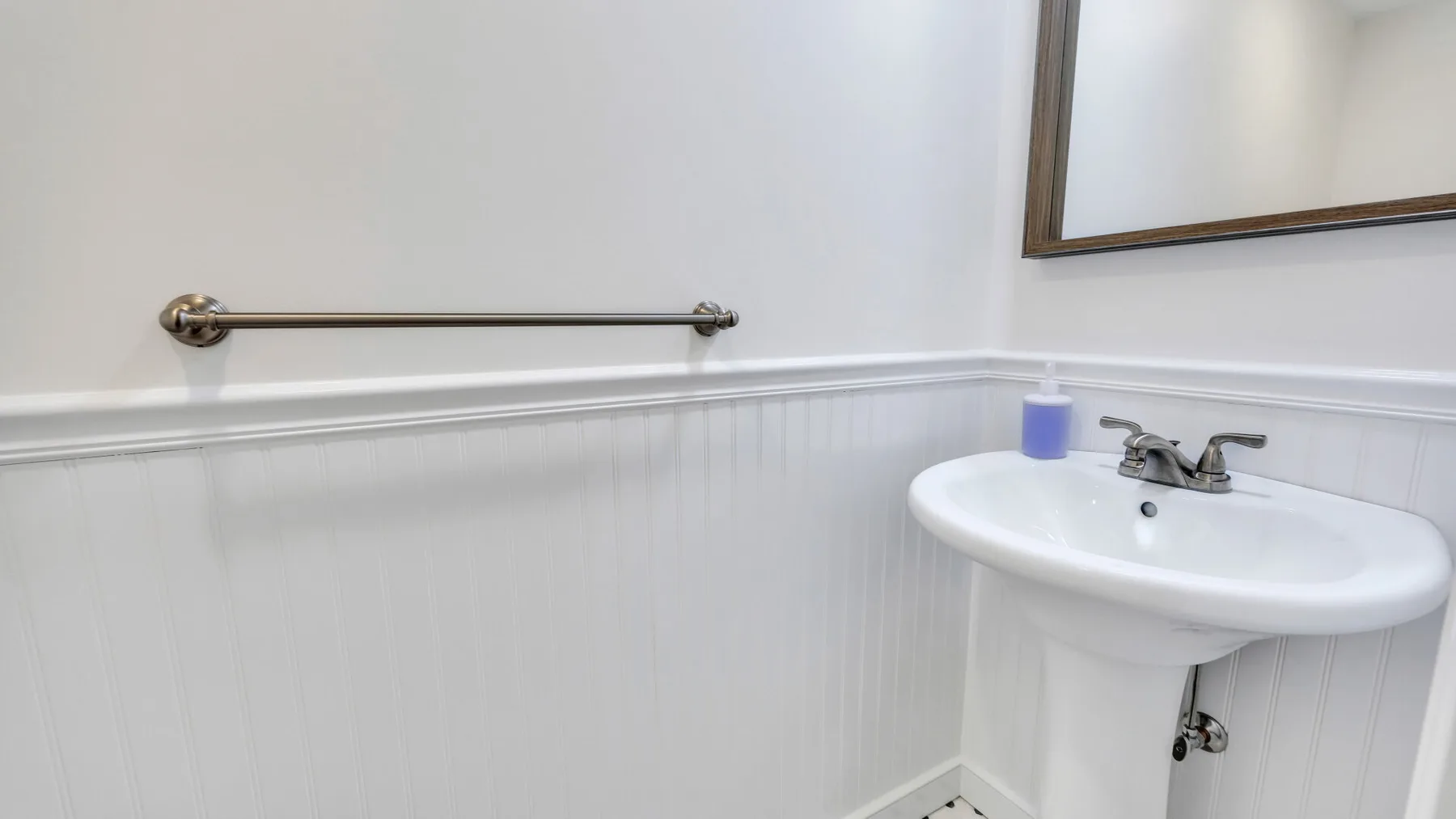 A bathroom sink sits beneath a mirror, with a towel bar on the wall.