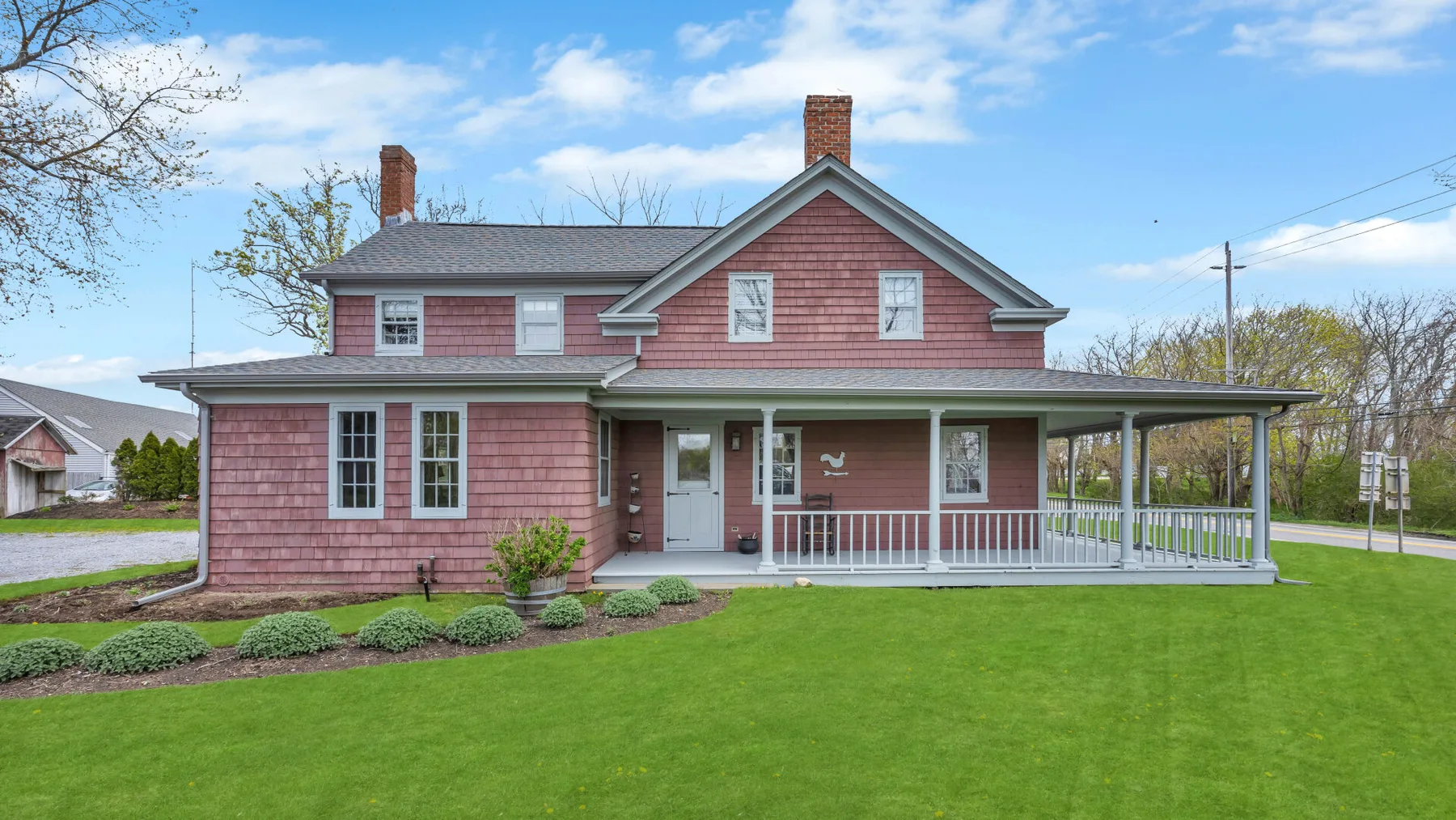 A red two-story house with a covered porch stands beside a broad green lawn.
