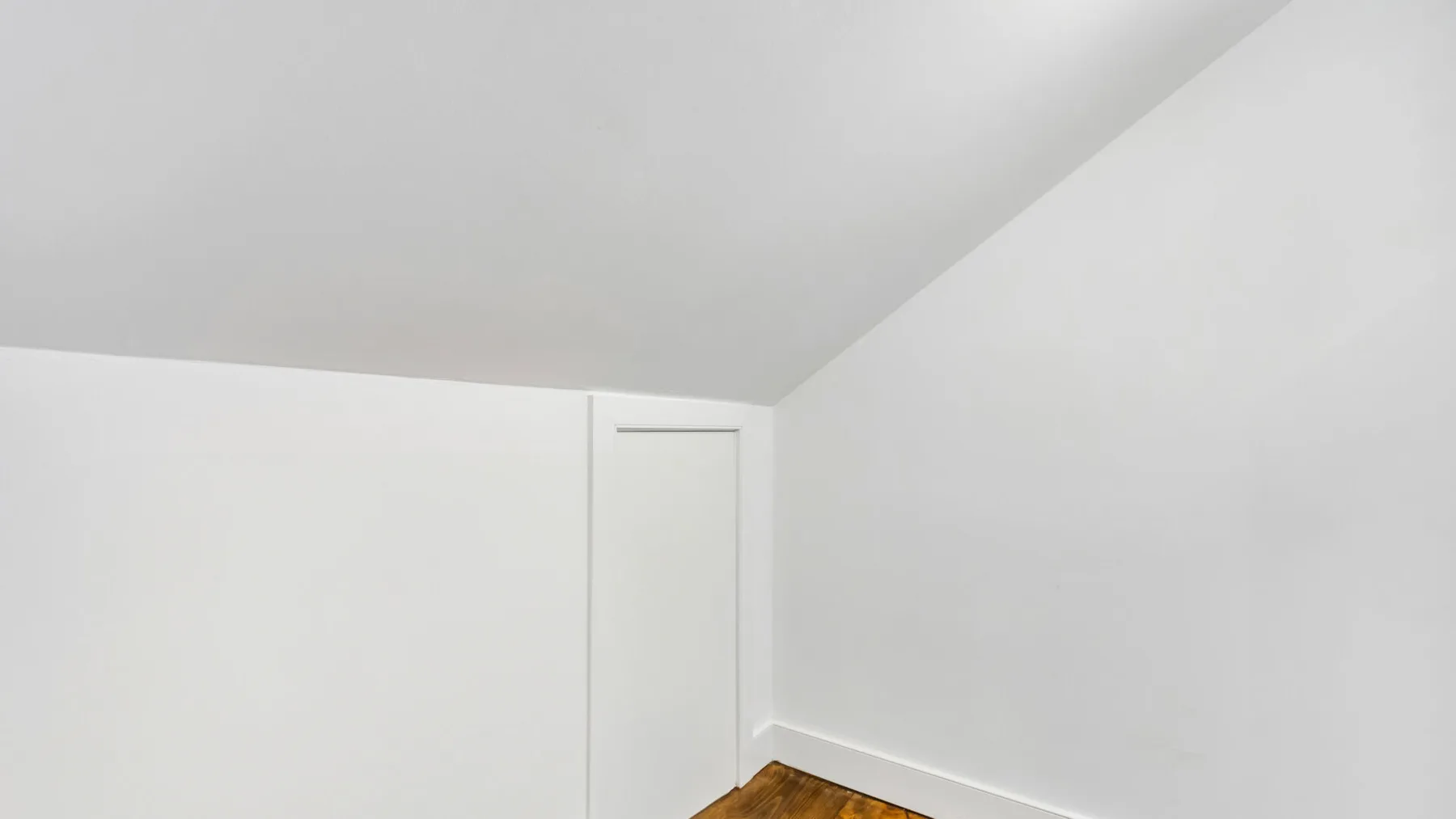 A small attic room with sloped ceilings and a closed door.