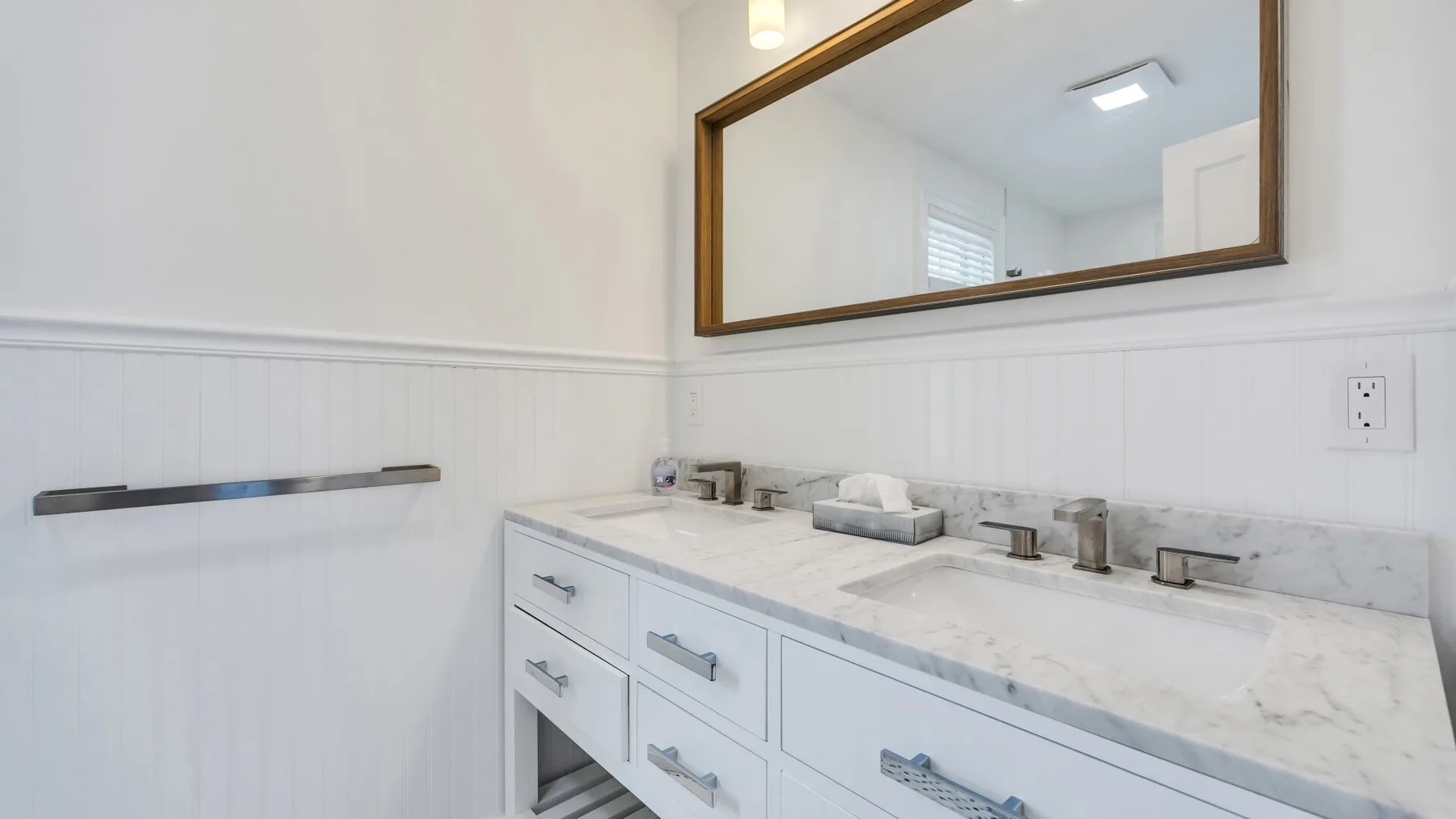 A bright bathroom vanity with a wide mirror and two sinks.