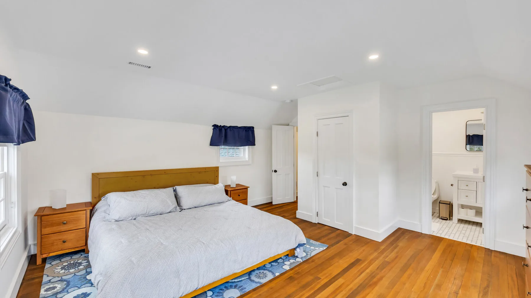 A bedroom with a large bed, wooden nightstands, and hardwood flooring.