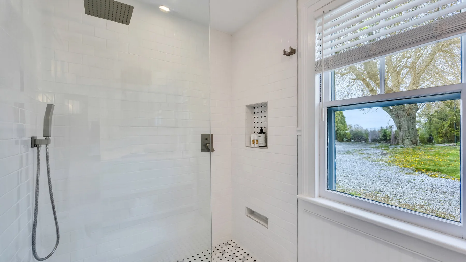 A bright tiled shower area with a window overlooking greenery.