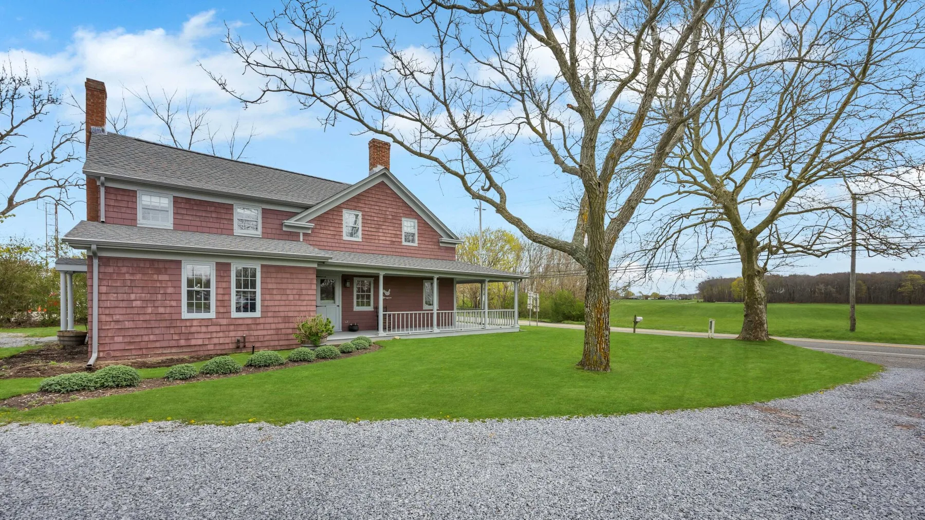 A red two-story house stands beside a gravel driveway and green lawn.