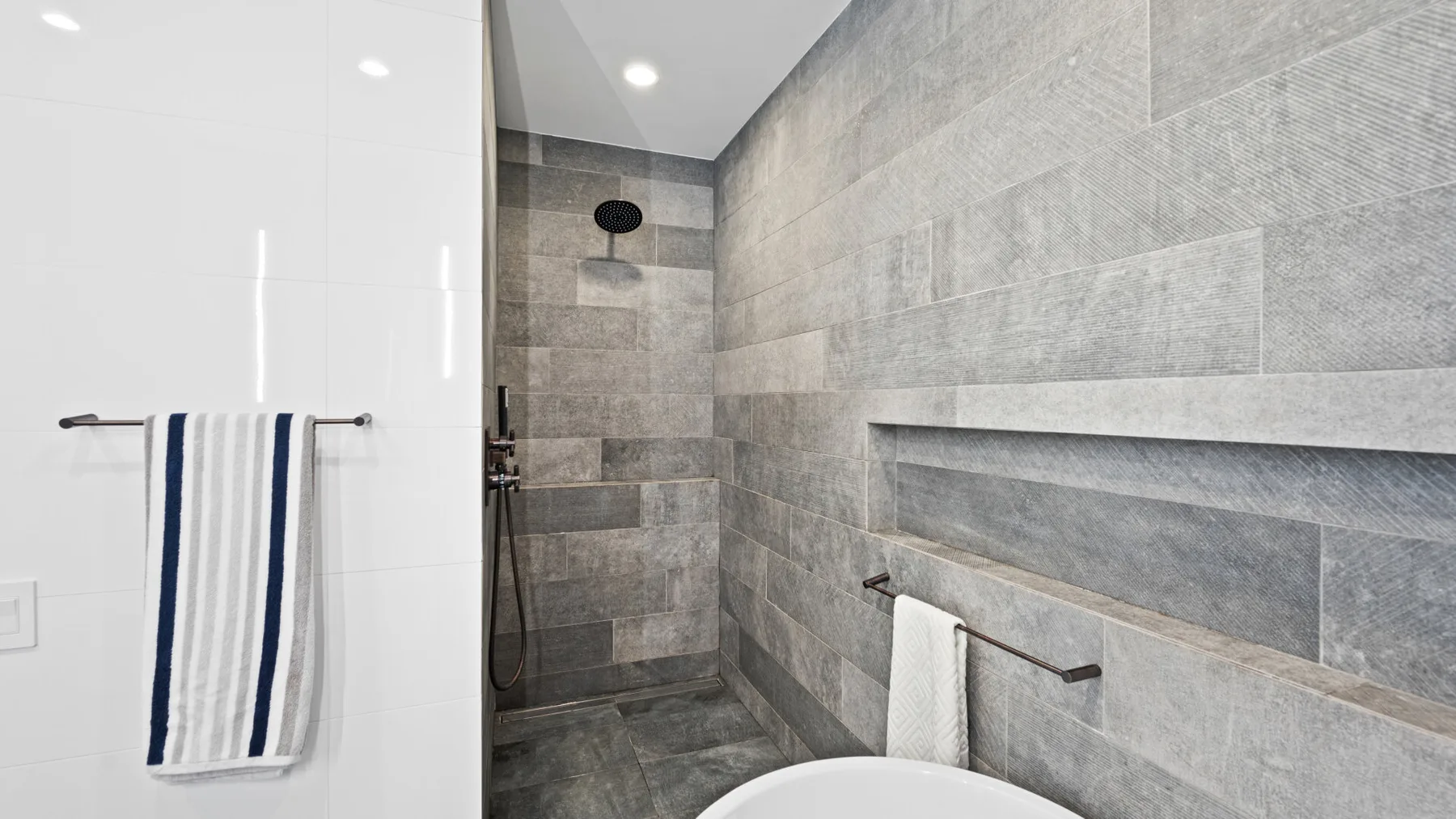 A tiled bathroom shower area with a towel hanging on a rail.
