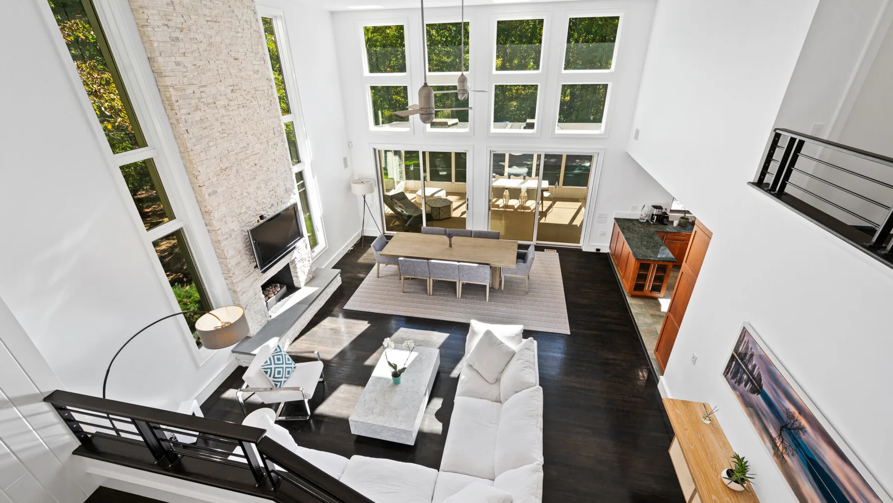 A bright living room has a high ceiling, large windows, and seating around a coffee table.