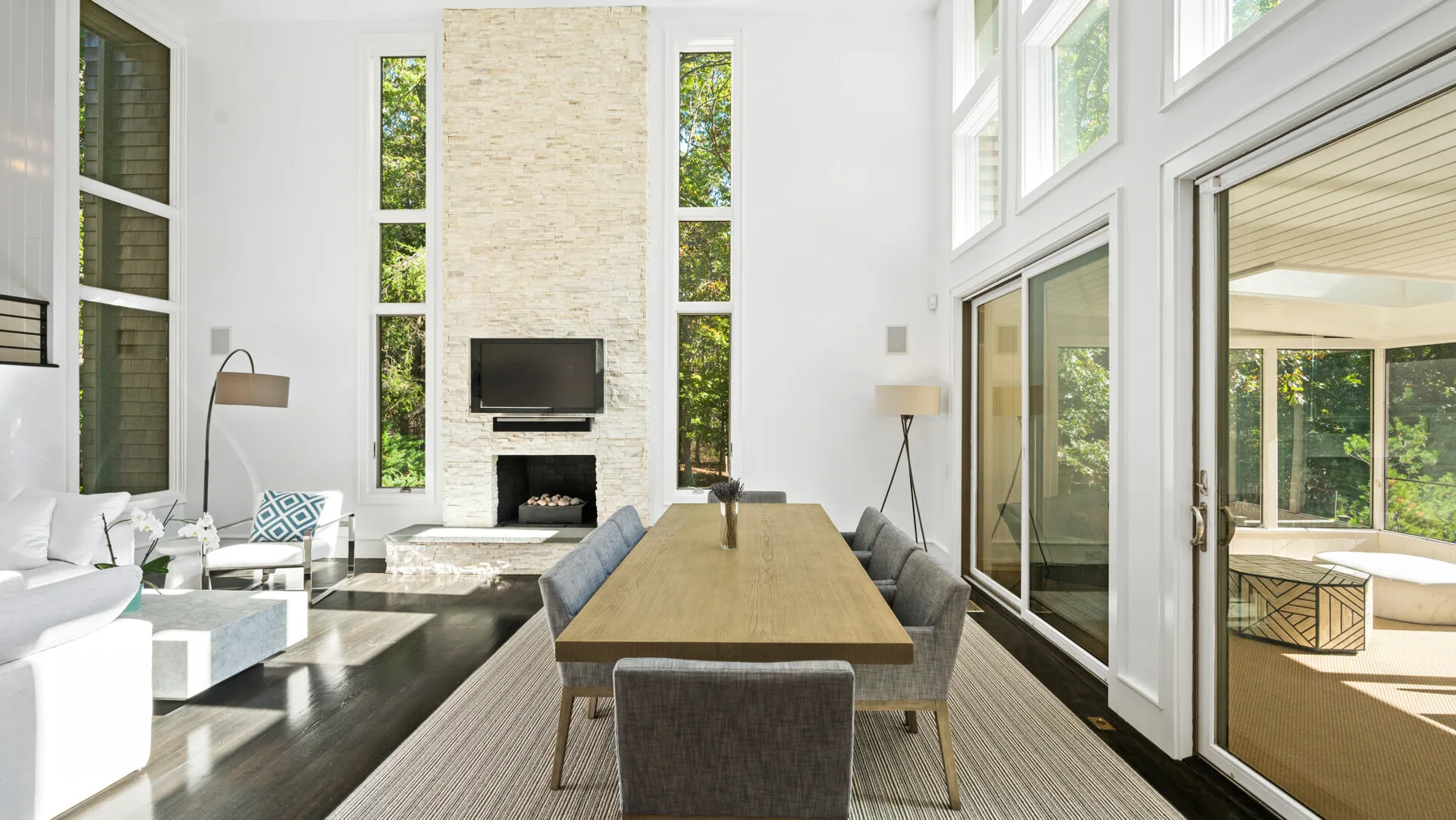 A bright living and dining room with a long table beside large windows.
