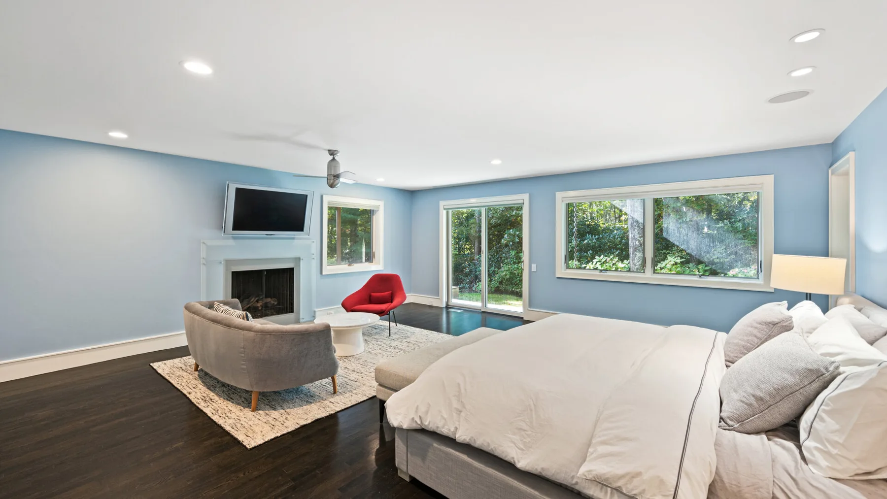 A bedroom with a large bed, a seating area, and wide windows.