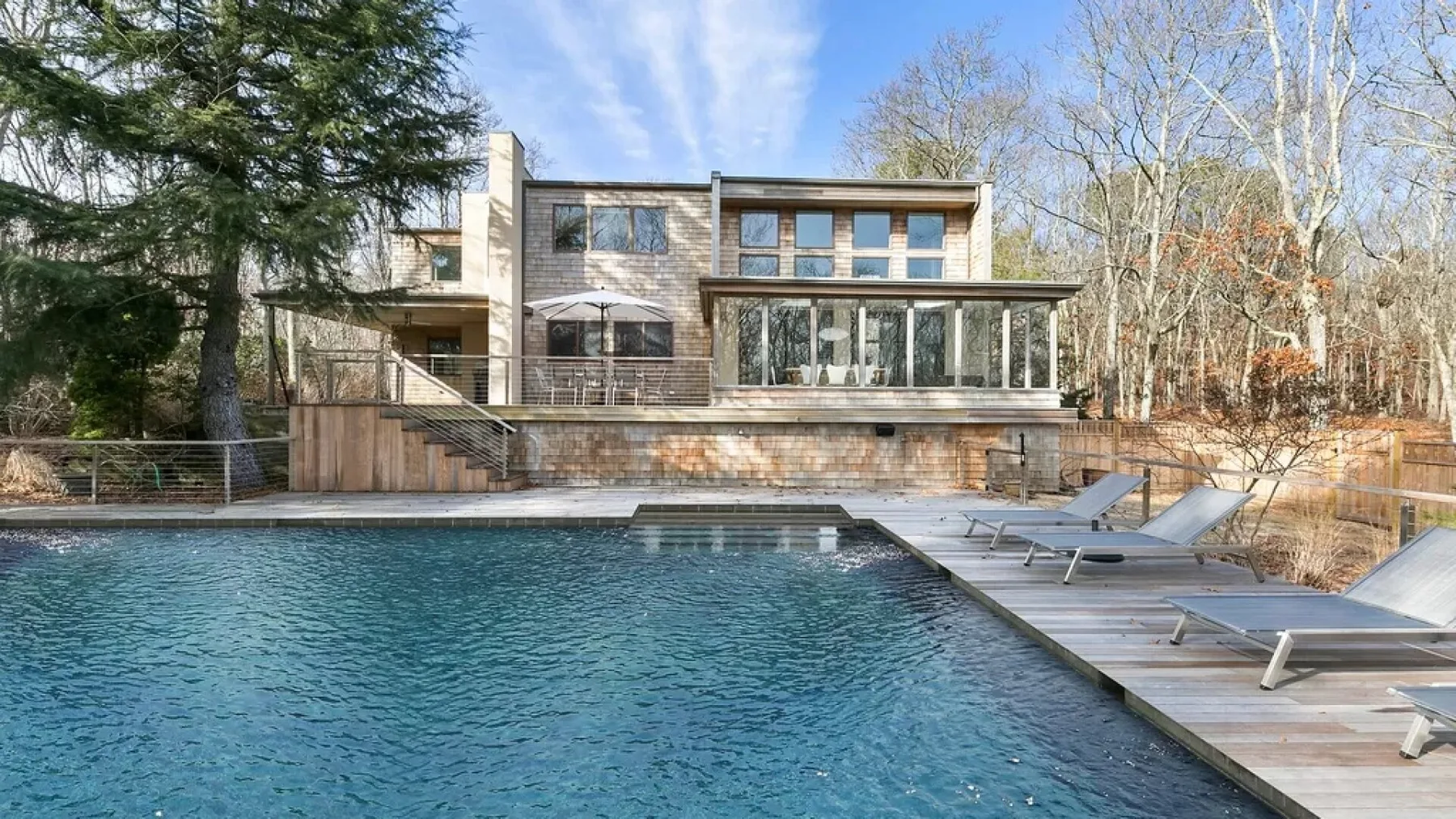 A modern house overlooks an outdoor swimming pool and deck seating.