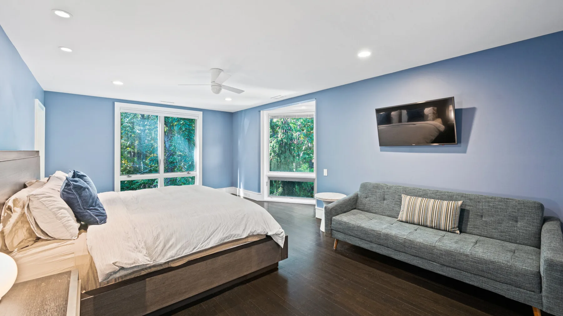 A bedroom with a bed and gray seating beside large windows.