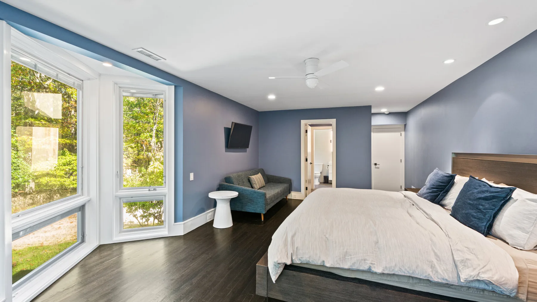 A bedroom with a large bed and bright windows overlooking greenery.