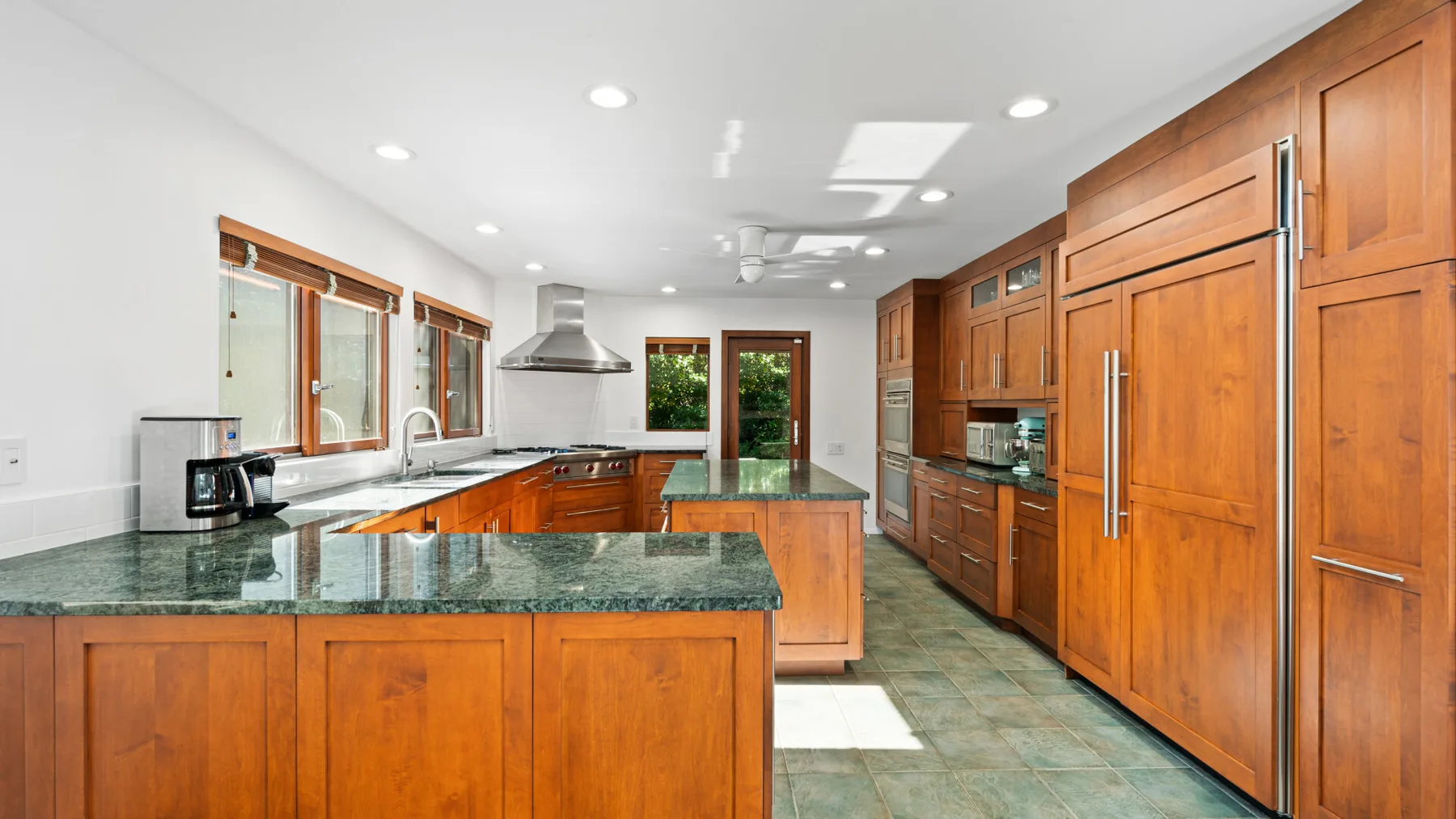 A spacious kitchen with wooden cabinets, green countertops, and a central island.