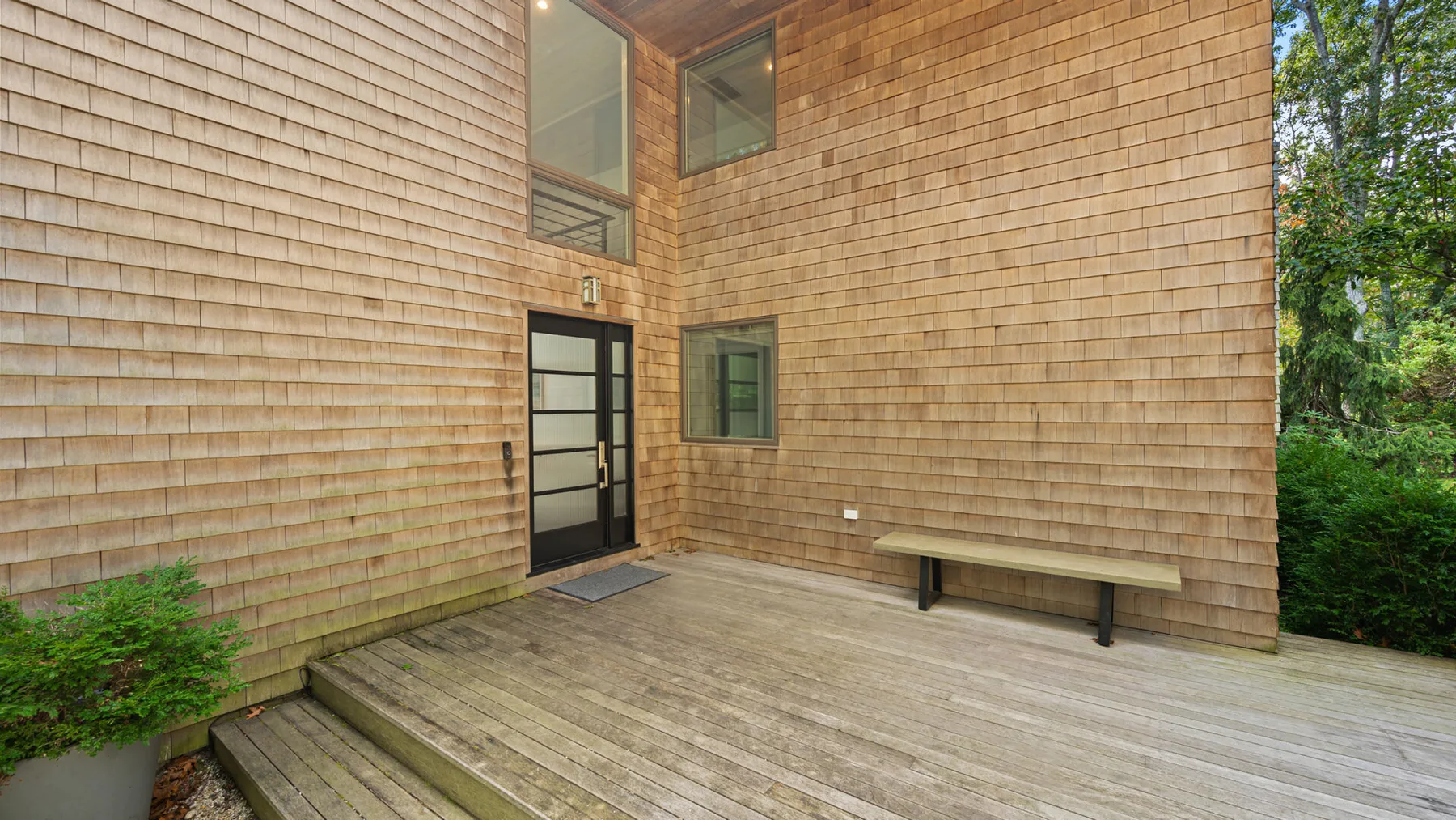 A wooden deck beside a building with shingle-clad walls and a dark door.