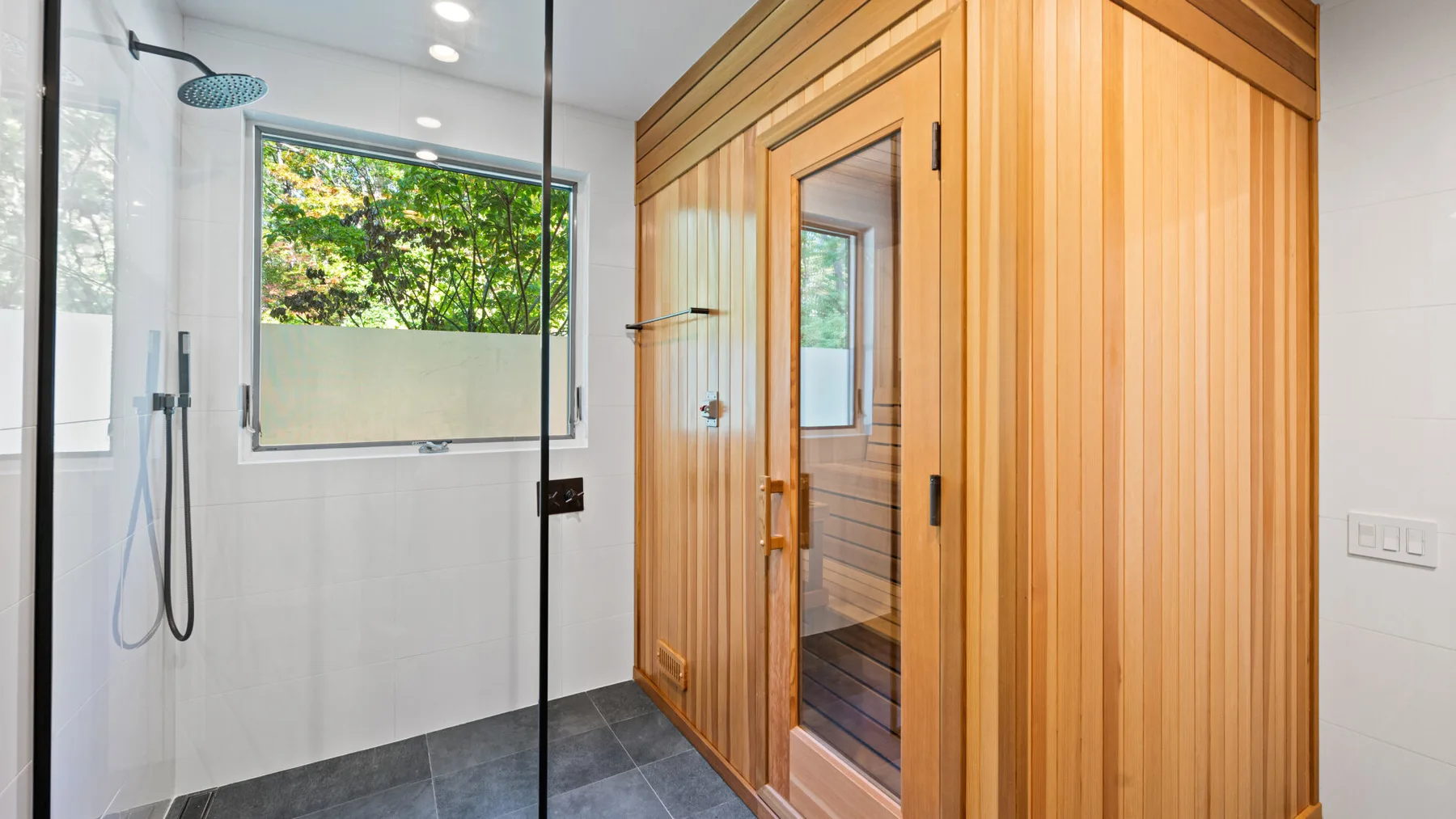 A bright bathroom with a glass shower and a wooden sauna enclosure.