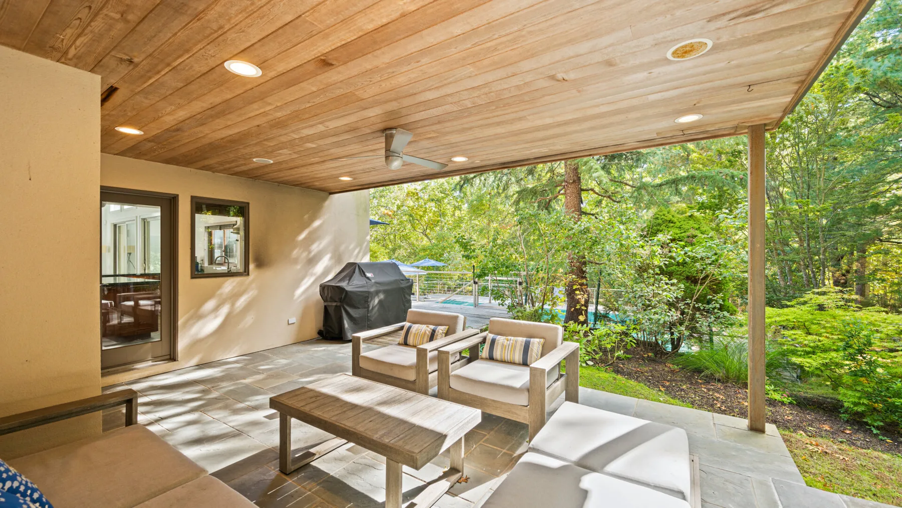 A covered patio with cushioned seating and a wooded view.