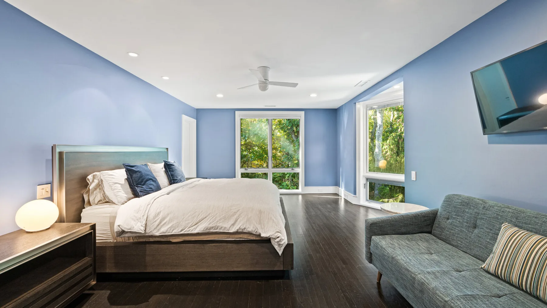 A bedroom with a bed, a seating area, and large windows.