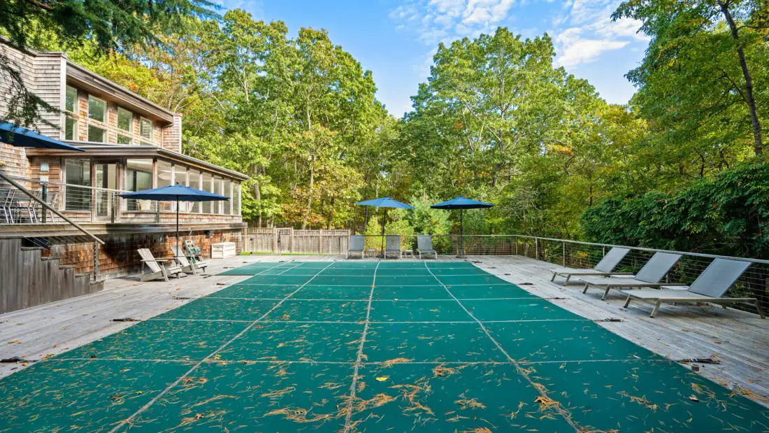 An outdoor swimming pool is surrounded by a wooden deck and leafy trees.