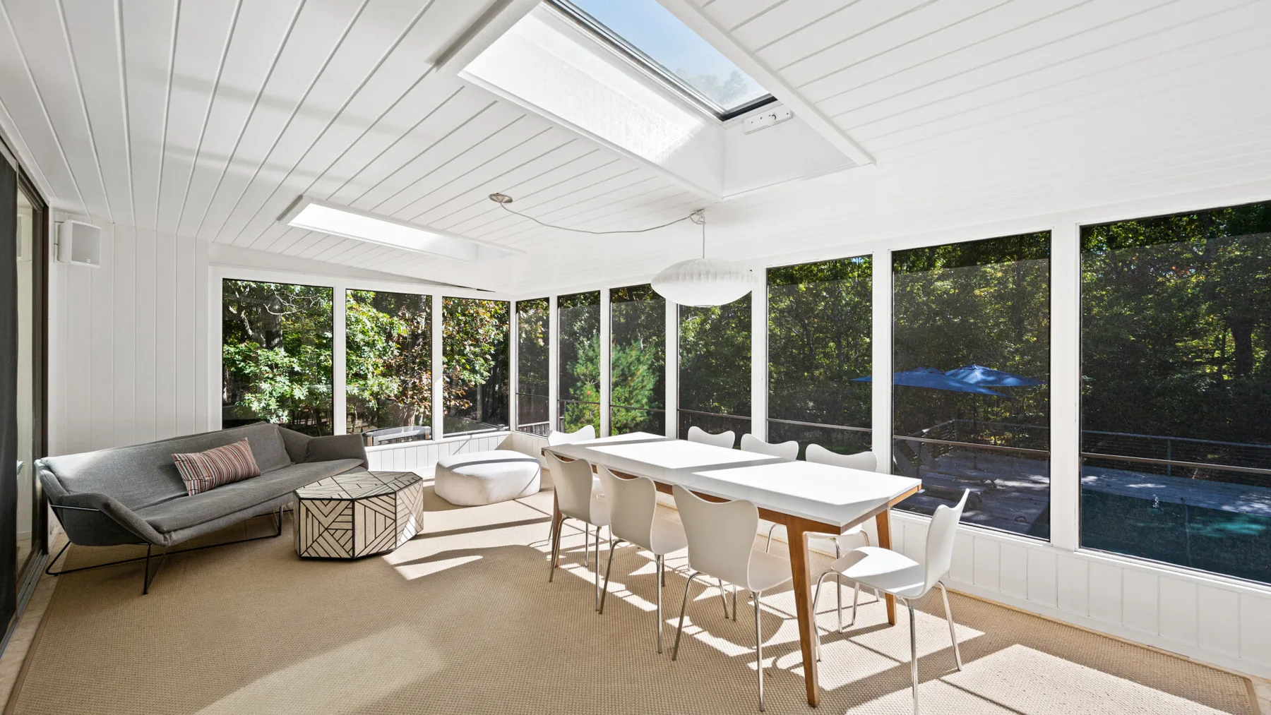 A bright enclosed dining area with a long table, chairs, and large windows.