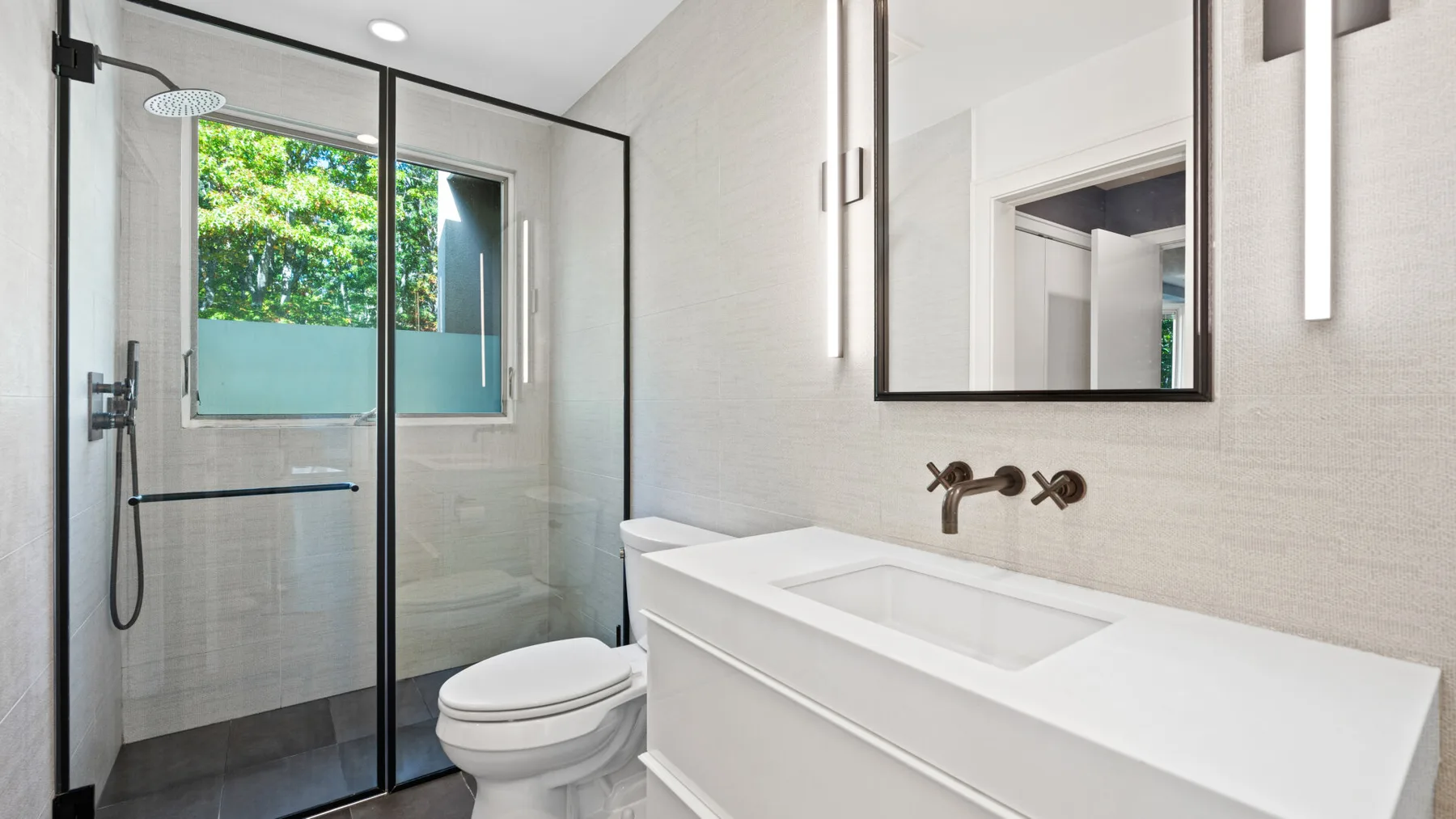 A bright bathroom with a glass shower, toilet, and white vanity.