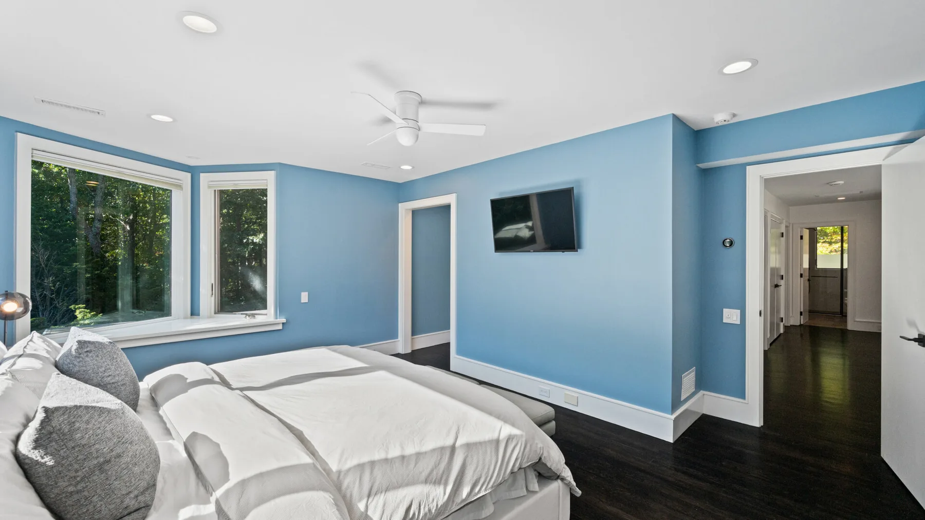 A bedroom with a bed, blue walls, and large windows overlooking trees.