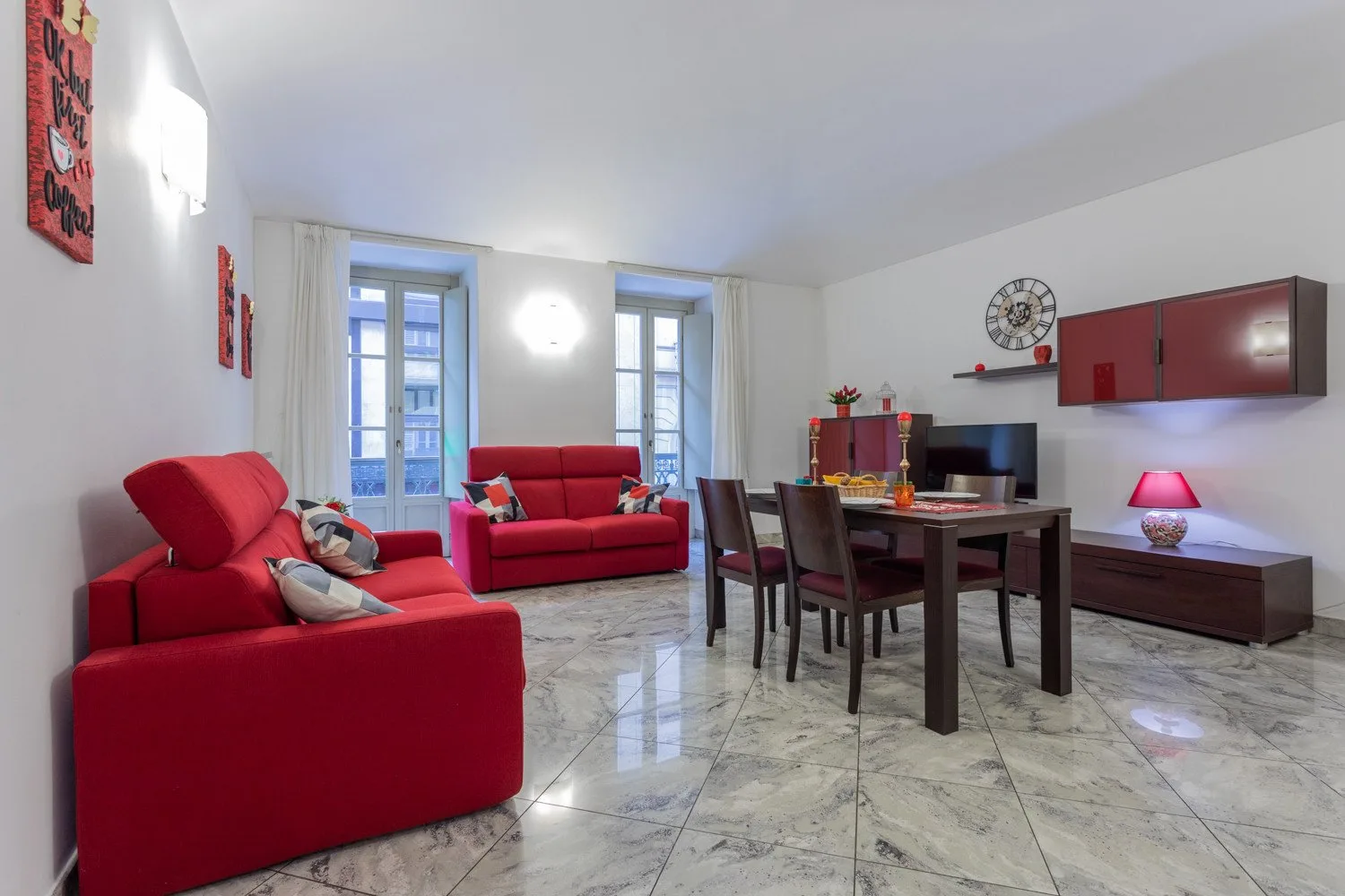 A bright living and dining room with red seating around a dark dining table.