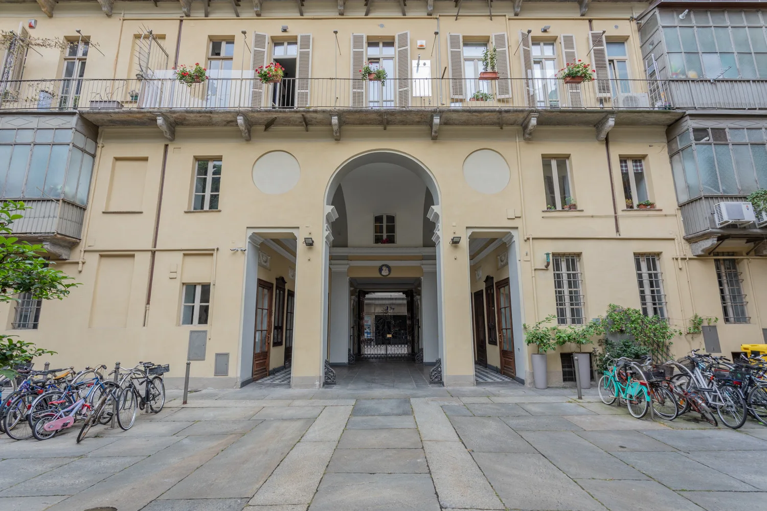 A courtyard entrance beneath a pale multi-story facade, with bicycles along both sides.