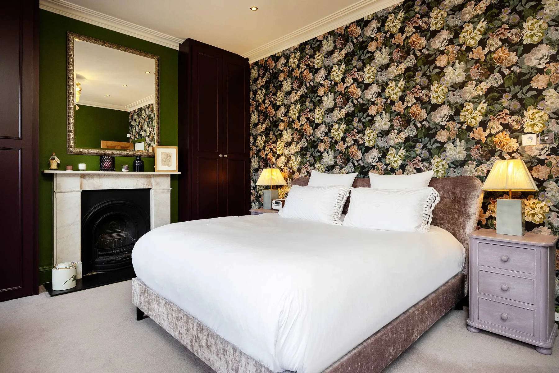 Un dormitorio con una cama grande, papel tapiz floral y una chimenea.