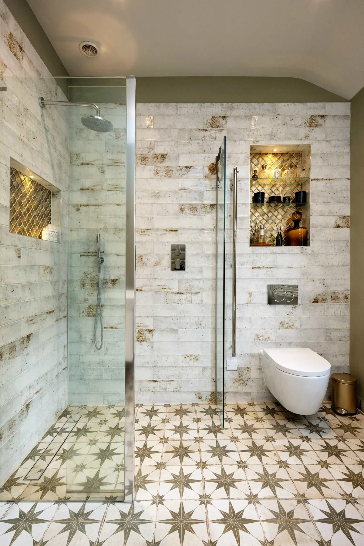 Baño revestido de azulejos con ducha de vidrio y nichos en la pared.